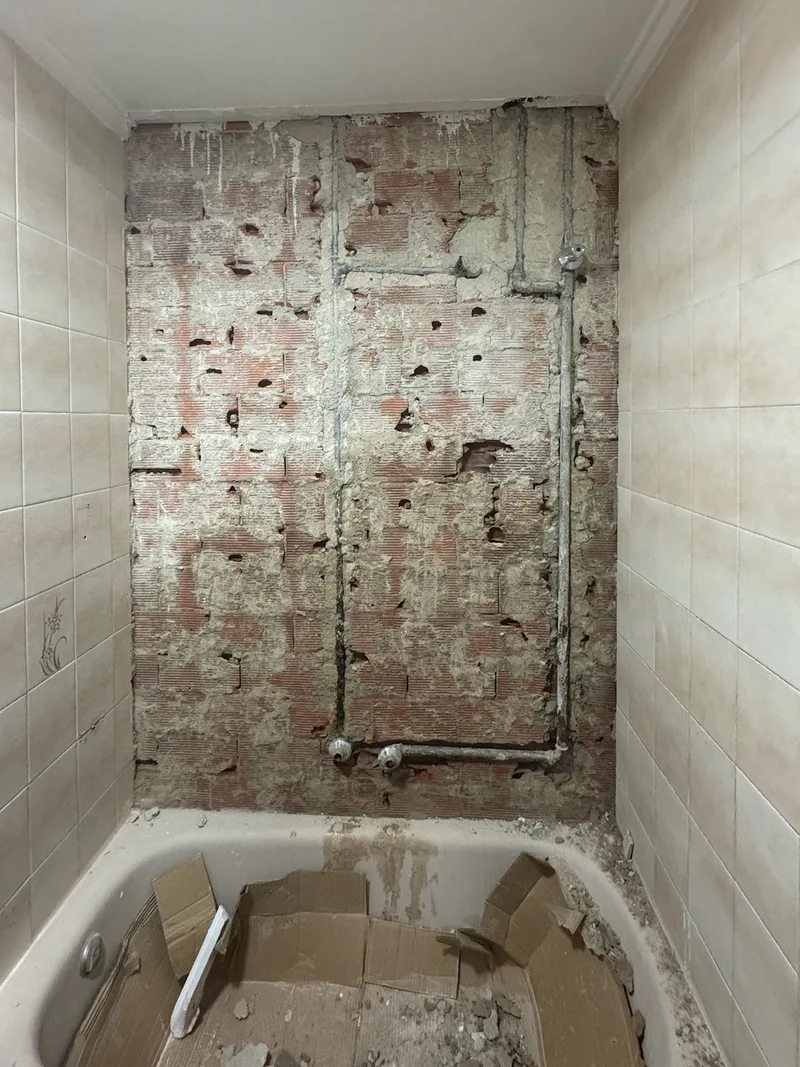 Antes: Pared de la bañera picada hasta el ladrillo, con tuberías a la vista y escombro en la bañera