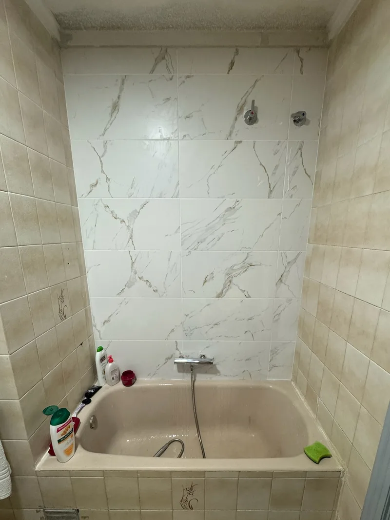 Después: Pared de la bañera revestida con porcelánico blanco efecto mármol y grifería nueva
