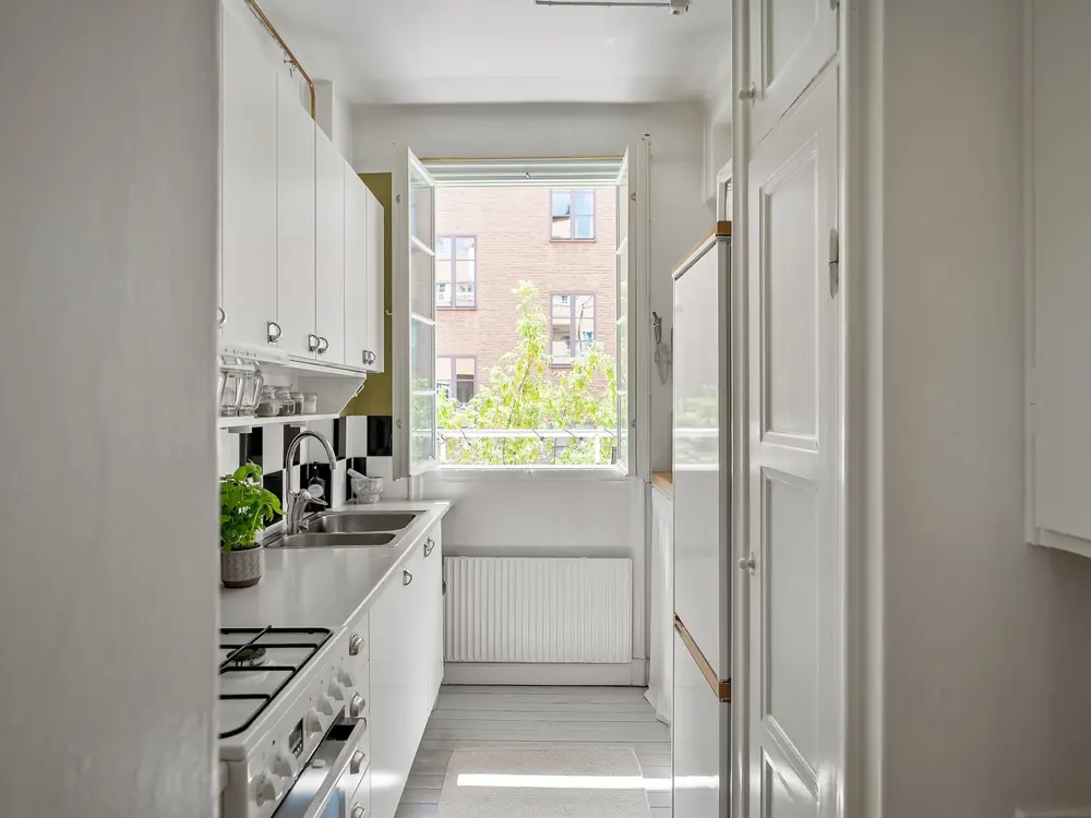 Después: Cocina reformada con muebles blancos, encimera clara y ventana al fondo (imagen de muestra)