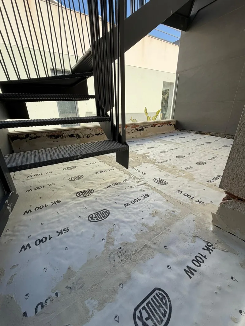 Antes: Patio bajo la escalera metálica cubierto con lámina impermeabilizante
