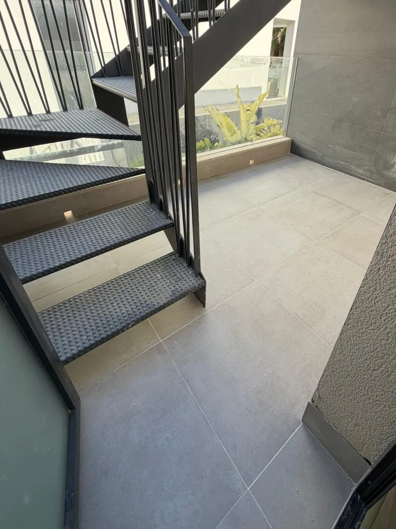 Después: Patio terminado con porcelánico gris bajo la escalera metálica