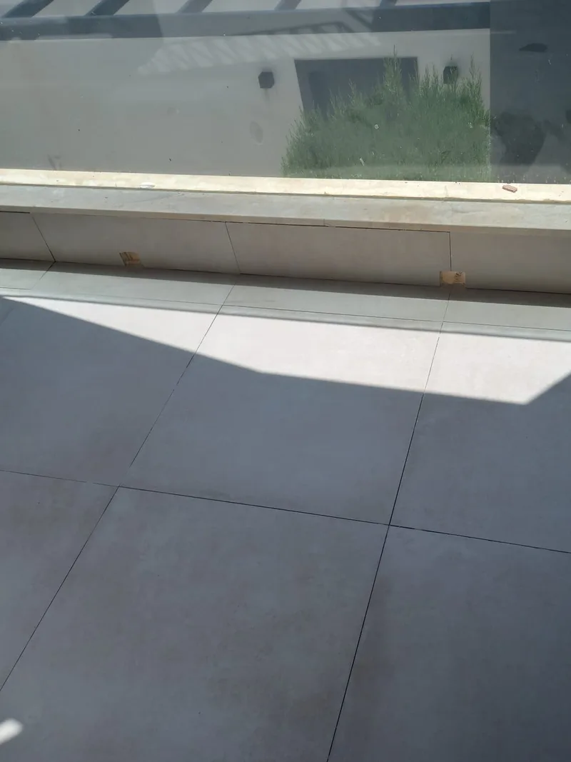 Después: Terraza terminada con porcelánico gris claro de gran formato y murete rematado bajo la barandilla de vidrio