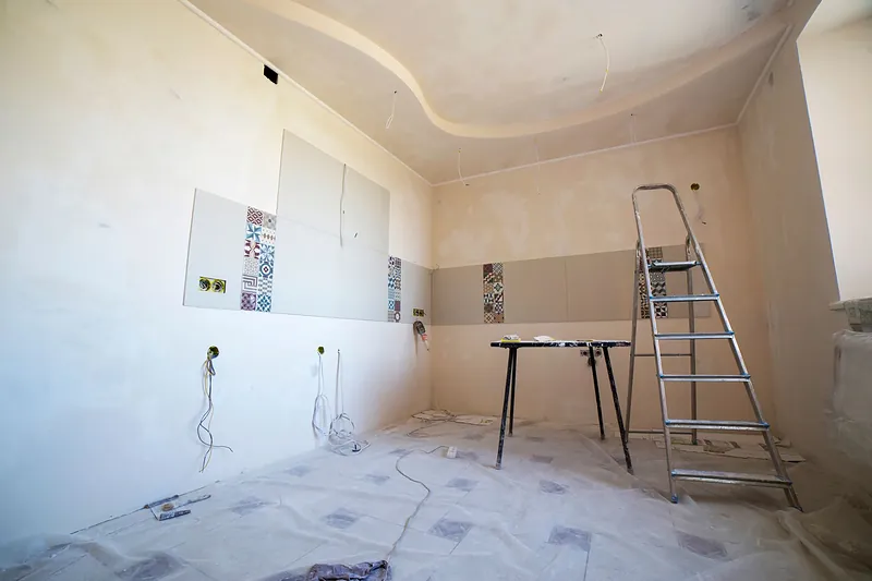 Cocina en obra con el alicatado a medias, tomas de agua y cajas eléctricas a la vista y el suelo protegido
