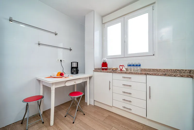 Cocina de piso reformada con muebles blancos, encimera de granito y alicatado blanco hasta el techo