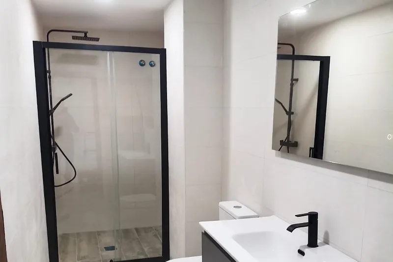 Baño reformado con ducha de mampara negra, mueble de lavabo gris suspendido y espejo