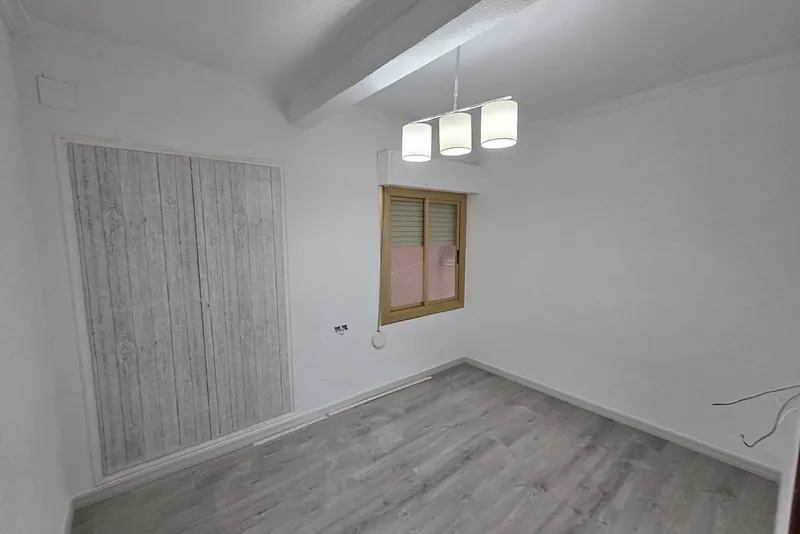 Dormitorio reformado con paredes blancas, suelo laminado gris, viga y lámpara de tres pantallas