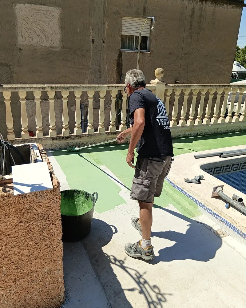 Operario de Vertika Obras aplicando con rodillo pintura impermeabilizante junto a una piscina
