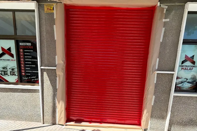 Persiana de local comercial recién lacada en rojo durante la obra, con el marco aún protegido con papel